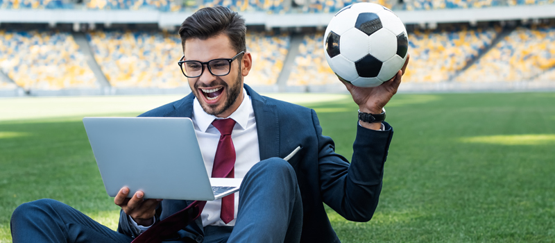 Homem com bola de futebol na mão e computador no colo